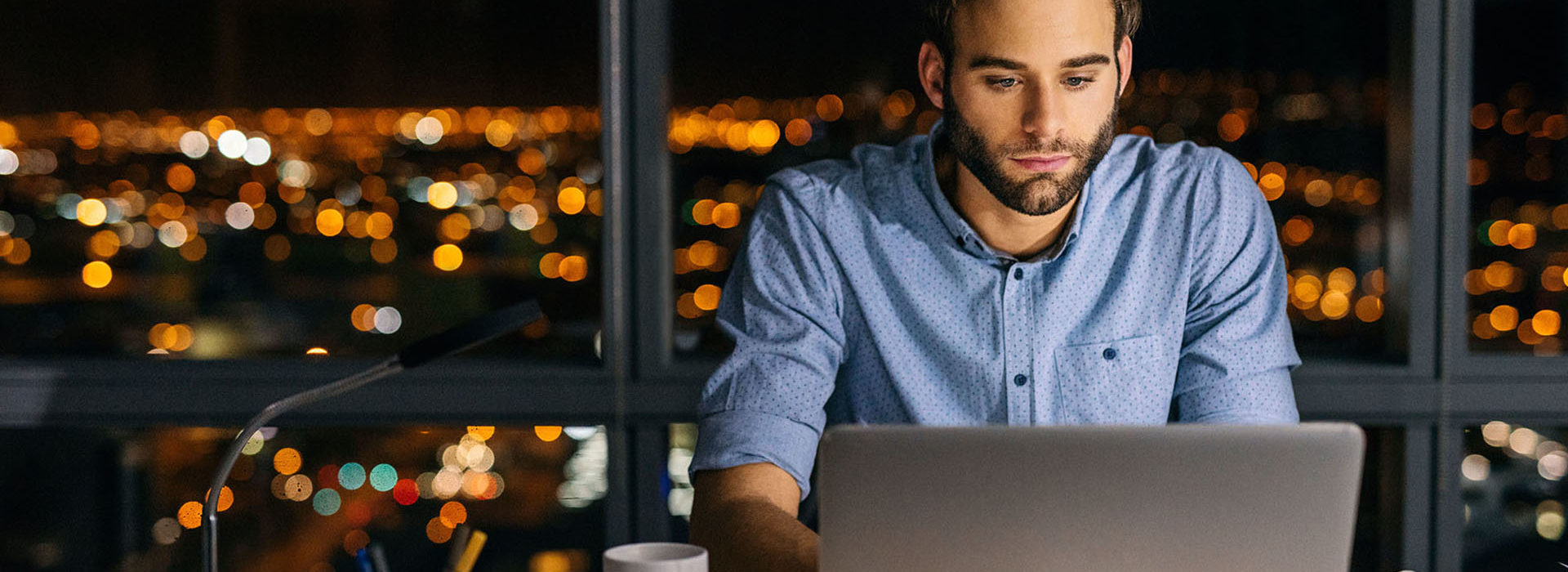Un homme à son bureau la nuit regardant son portail Ma Protection Sociale (MAPSO) sur son ordinateur Un homme à son bureau la nuit regardant son portail Ma Protection Sociale (MAPSO) sur son ordinateur