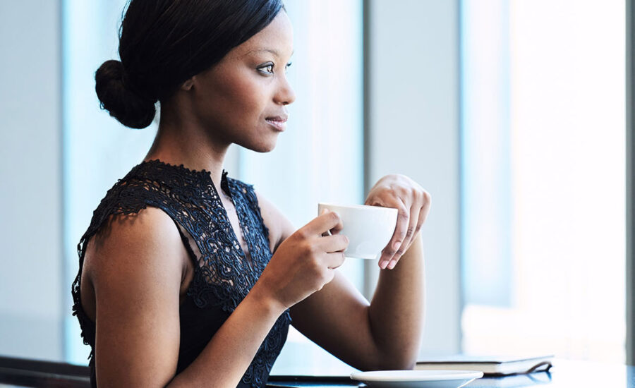 Une femme prenant son café au travail et regardant par la fenêtre