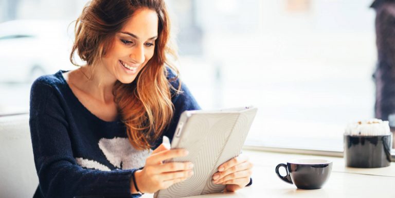 Une femme tenant sa tablette dans les main et prenant un café