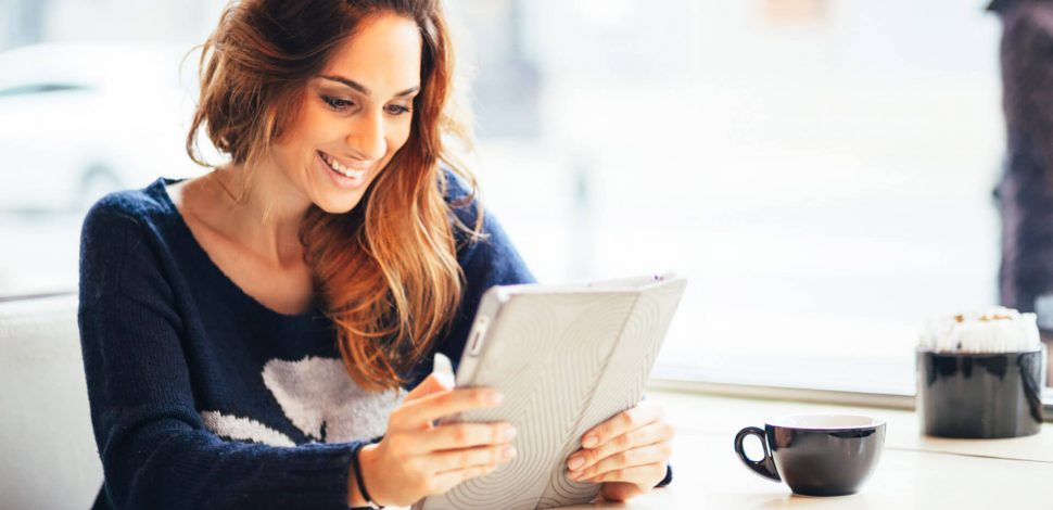 Une femme tenant sa tablette dans les main et prenant un café