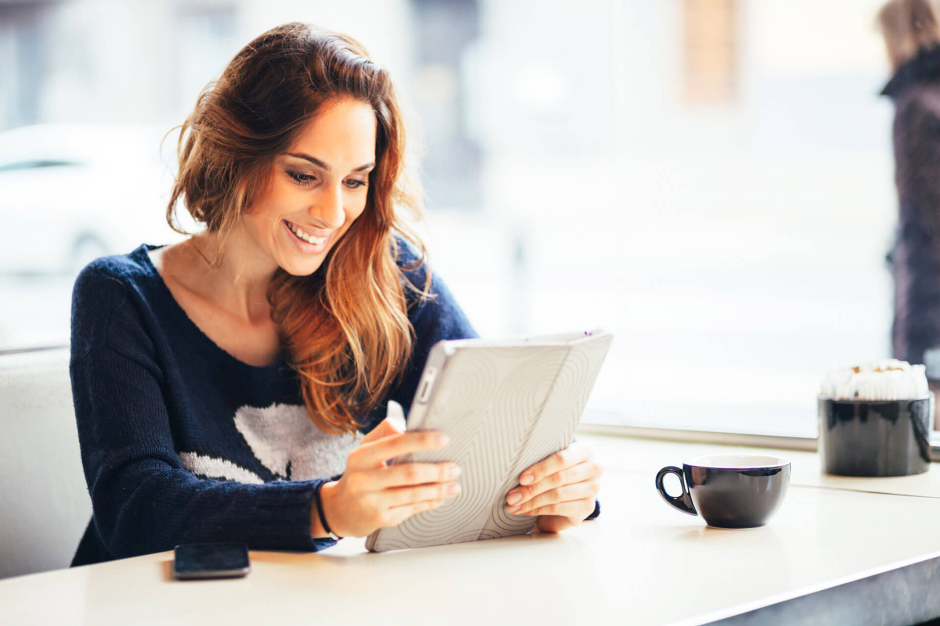 Une femme tenant sa tablette dans les main et prenant un café