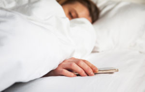 Une femme dans son lit en arrêt de travail dormant son portable à la main