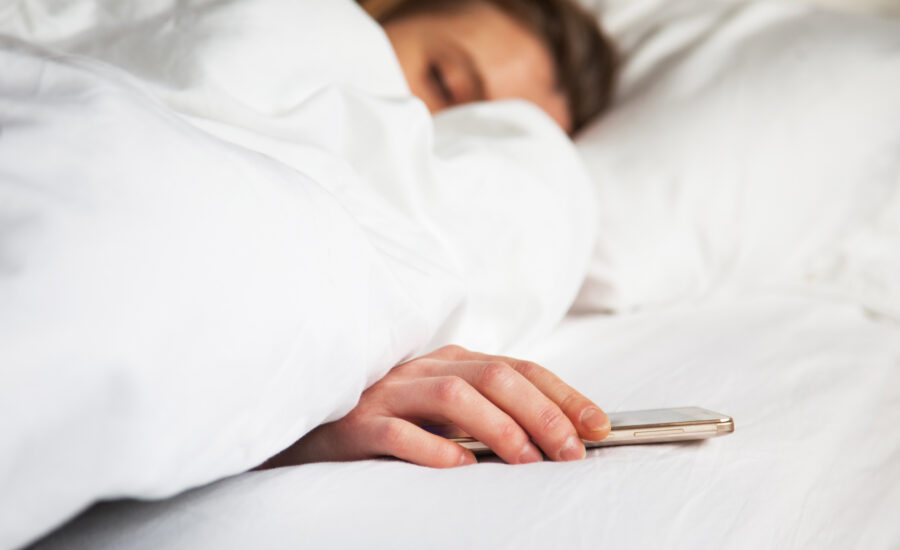 Une femme dans son lit en arrêt de travail dormant son portable à la main