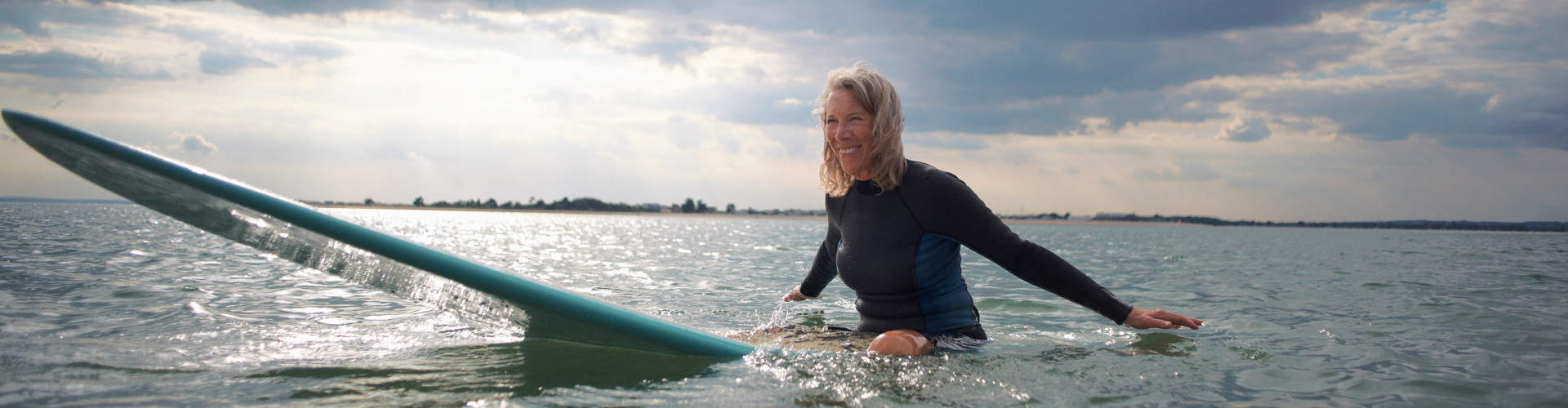 Vacationing abroad 2 Portrait of senior woman sitting on surfboard in sea, smiling