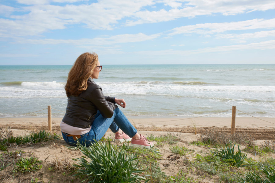 Une femme assise devant la mer regardant l'horizon - cancer Une femme assise devant la mer regardant l'horizon - cancer