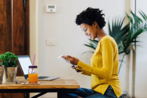 Une femme souriante assise à son bureau devant son ordinateur et avec une tablette pour regarder la vitrine digitale épargne retraite entreprise