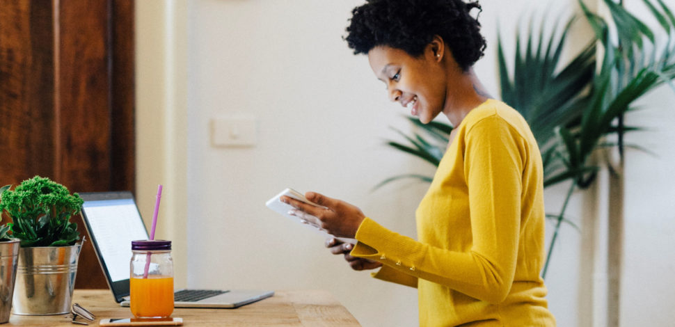 Une femme souriante assise à son bureau devant son ordinateur et avec une tablette pour regarder la vitrine digitale épargne retraite entreprise