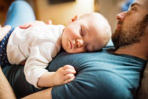 Un homme en congé paternité allongé et tenant son bébé dans les bras