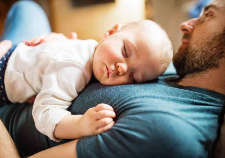 Un homme en congé paternité allongé et tenant son bébé dans les bras