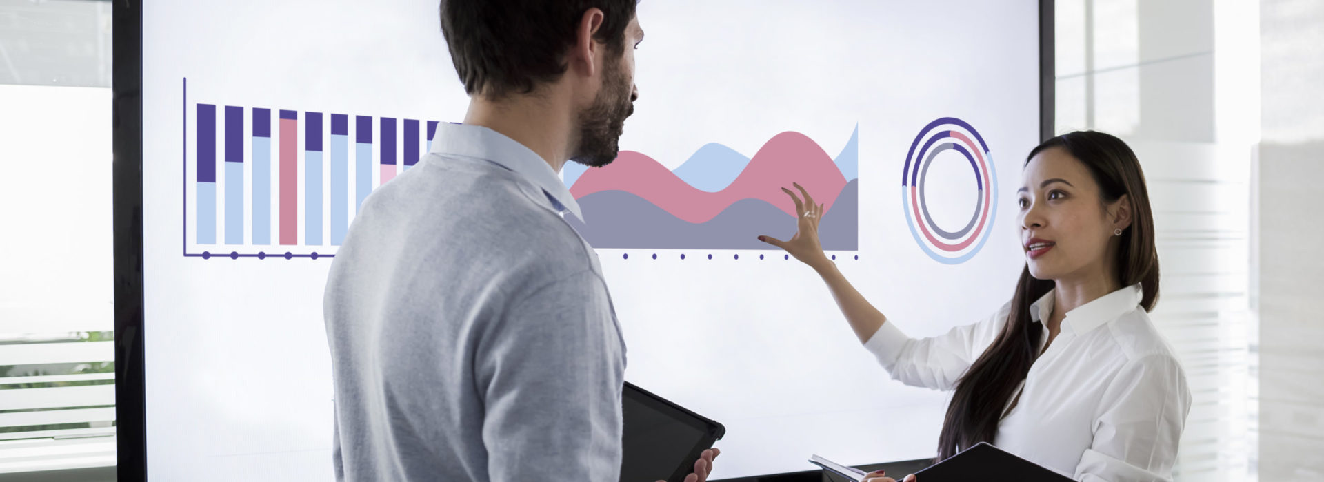 Male and female colleague discussing financial diagrams on large screen in meeting room and preparing for presentation Male and female colleague discussing financial diagrams on large screen in meeting room and preparing for presentation