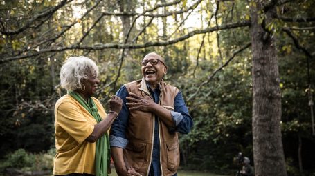 Un homme à moustache et une femme sénior rigolant ensemble dans le jardin