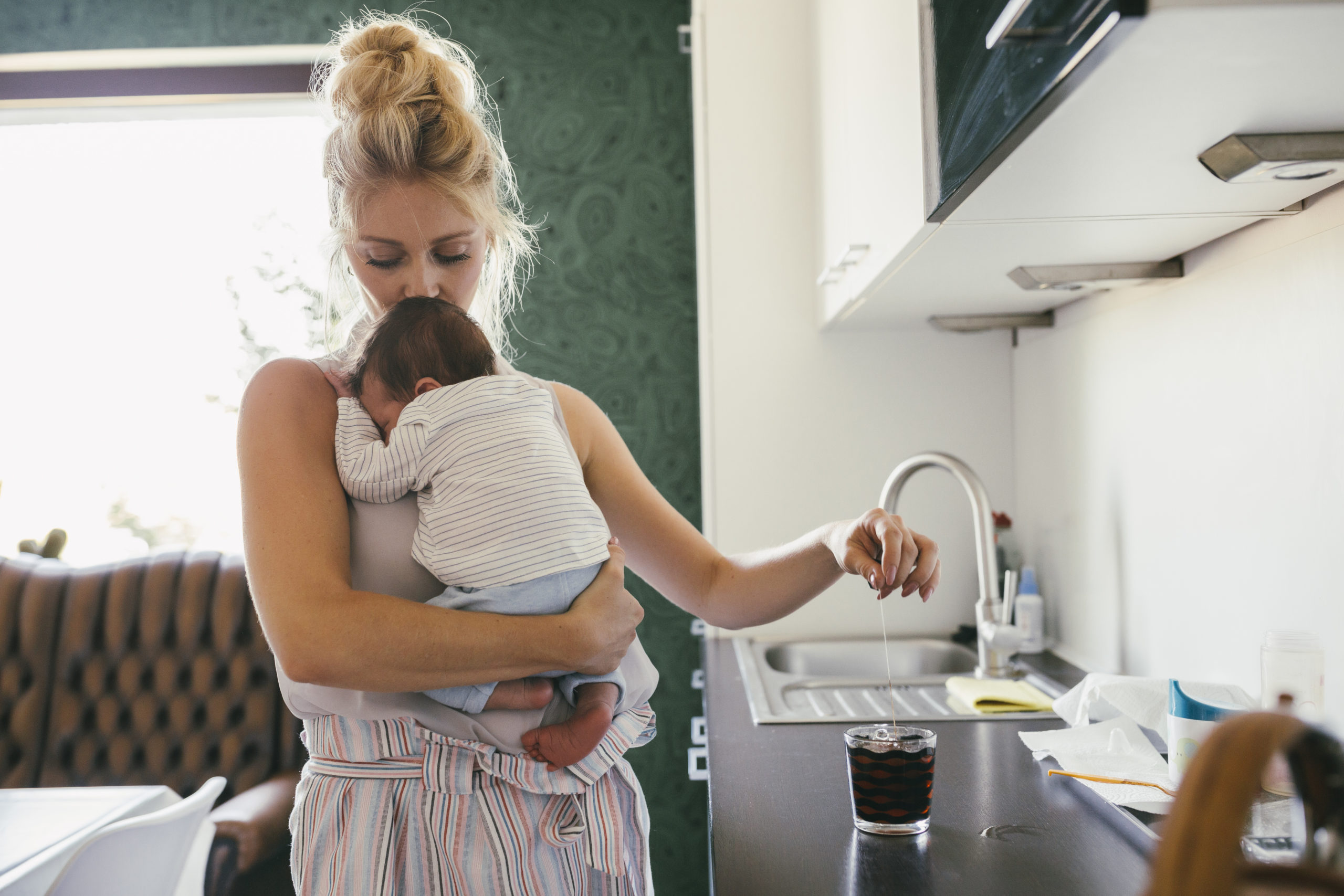 Une mère en congé maternité se préparant un café avec son bébé dans les bras