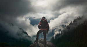 Un homme de dos portant un sac de randonnée et regardant les montagnes et la forêt - santé mentale