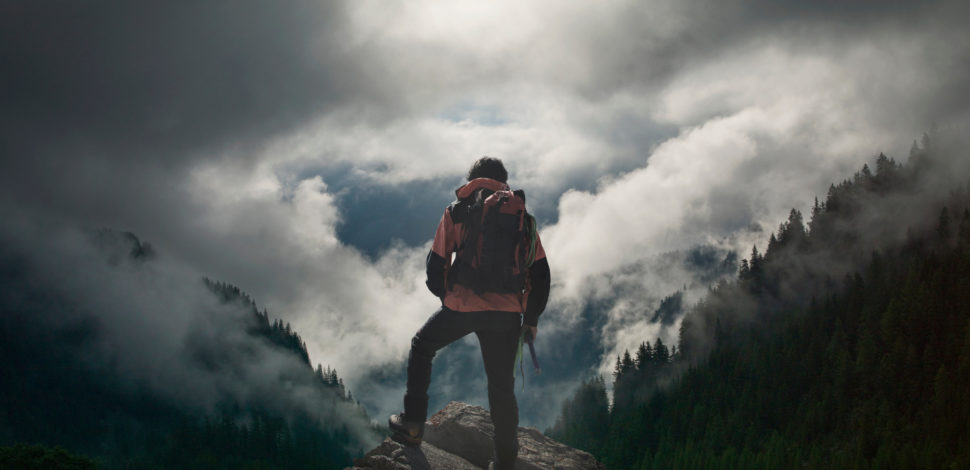 Un homme de dos portant un sac de randonnée et regardant les montagnes et la forêt - santé mentale