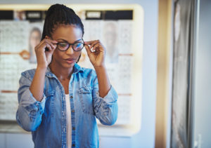 Une femme essayant des lunettes noires chez un opticien grâce à la réforme 100% santé