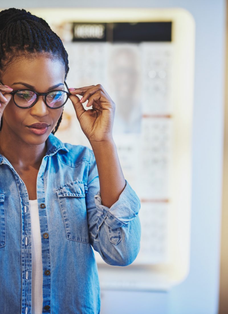 Une femme essayant des lunettes noires chez un opticien grâce à la réforme 100% santé