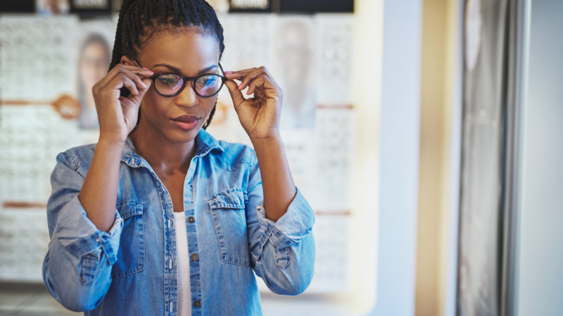 Une femme essayant des lunettes noires chez un opticien grâce à la réforme 100% santé