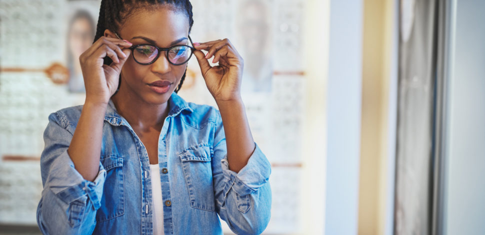 Une femme essayant des lunettes noires chez un opticien grâce à la réforme 100% santé