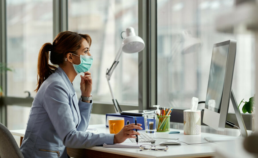 Une femme portant un masque et travaillant à son bureau devant son ordinateur - expatrié