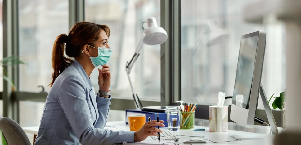 Une femme portant un masque et travaillant à son bureau devant son ordinateur - expatrié