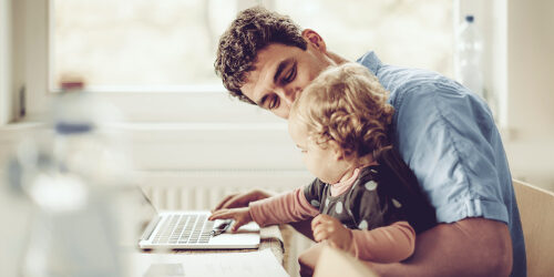 Un homme avec son enfant sur les genoux s'informant sur la fiche désignation bénéficiaire sur son ordinateur