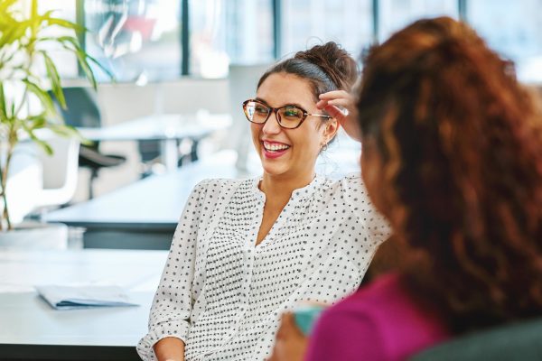 Une femme portant des lunettes discutant et rigolant lors d'une conversation au travail - qualité de vie au travail