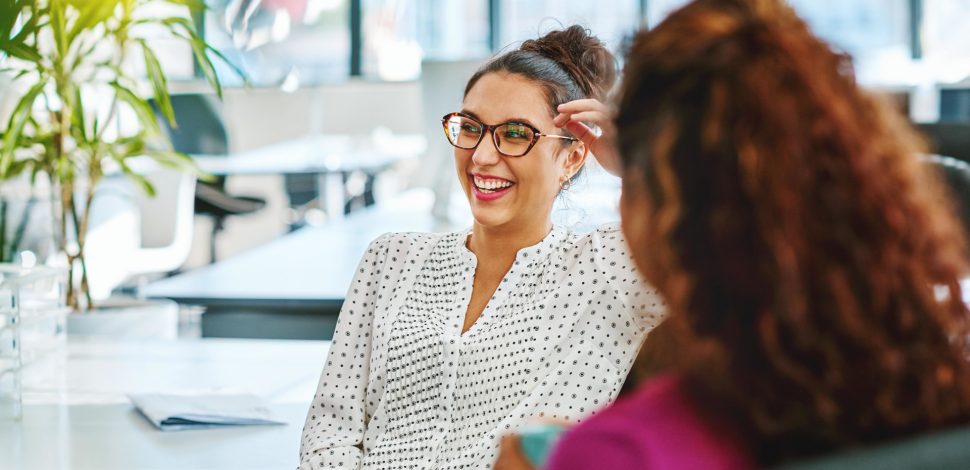 Une femme portant des lunettes discutant et rigolant lors d'une conversation au travail - qualité de vie au travail