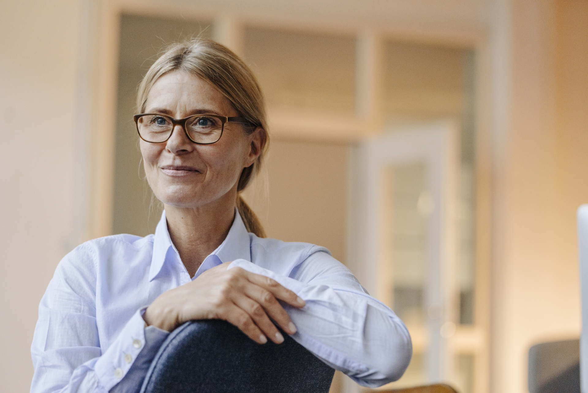 Une femme souriante portant des lunettes et assise sur une chaises