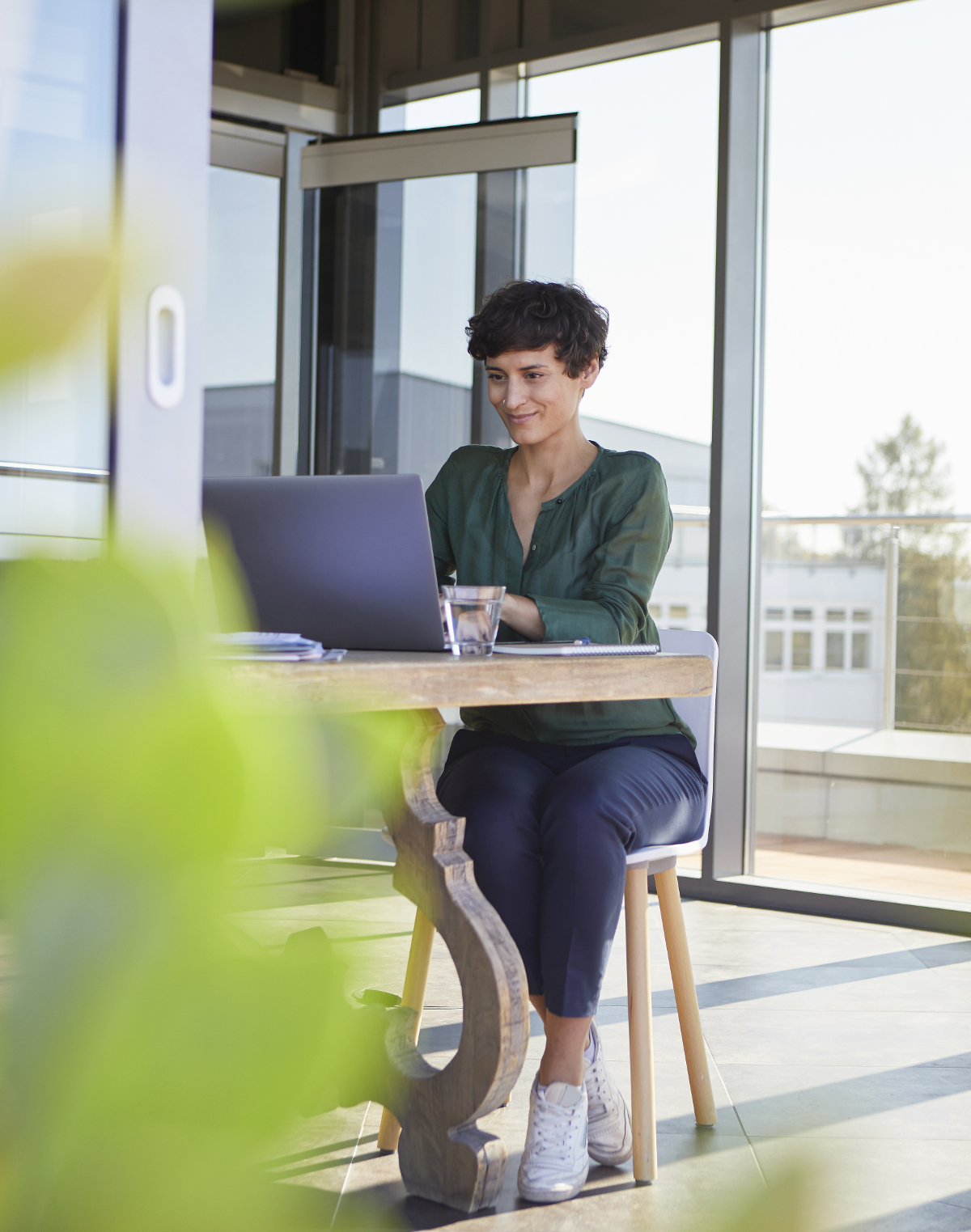 Une femme chez elle assise à une table dehors et utilisant son ordinateur portable