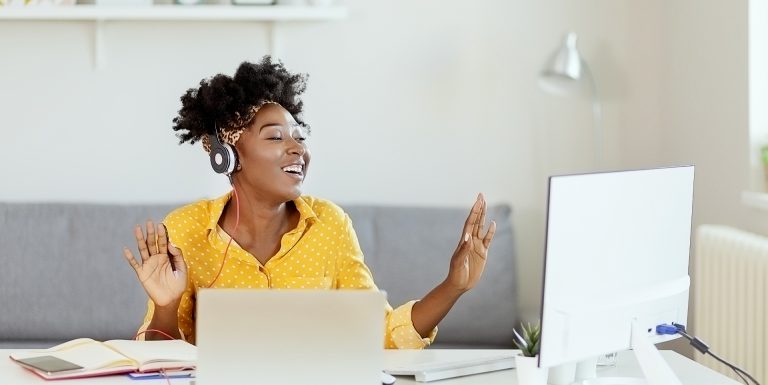 Une femme souriante devant son ordinateur et un casque écoutant la playlist Youtube ERE