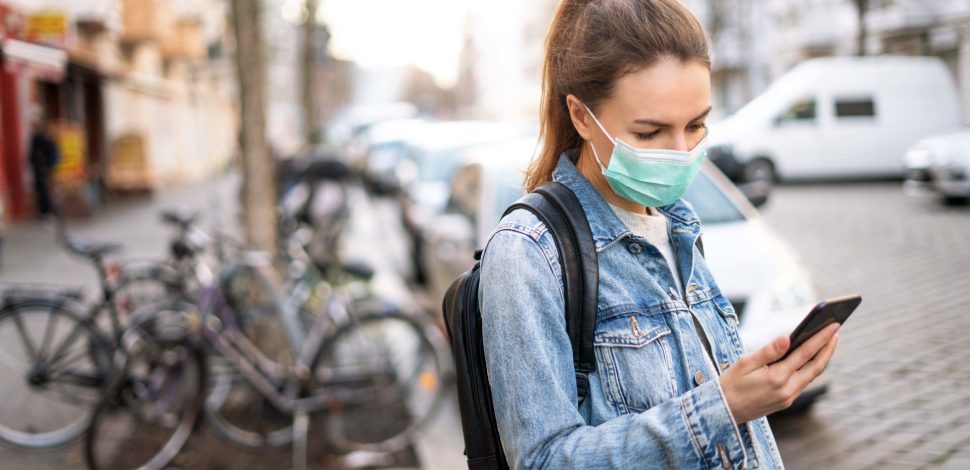 Une femme dans la rue portant un masque et regardant son téléphone portable