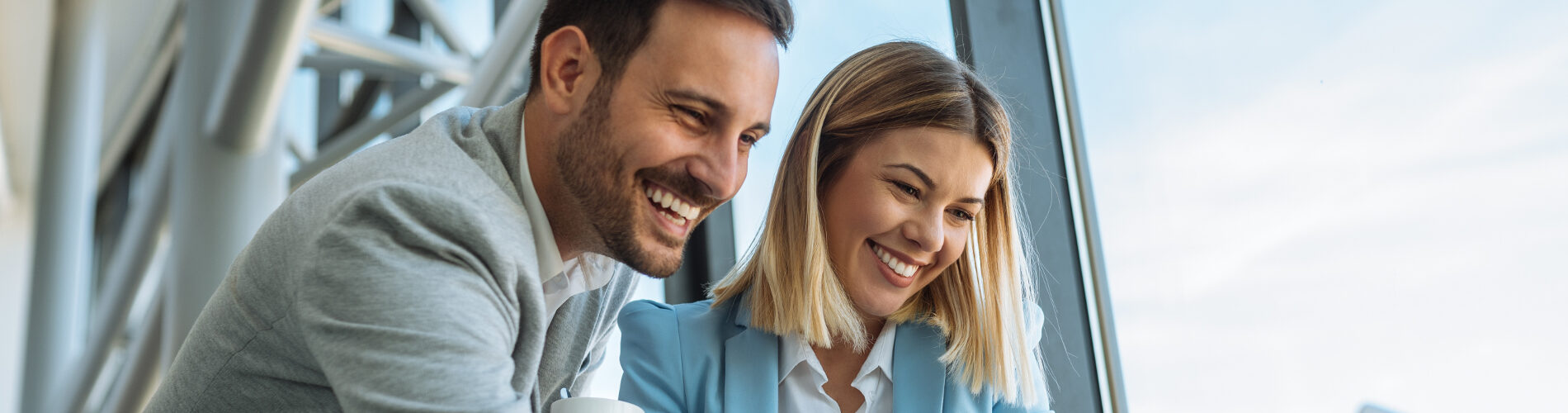 Un homme et une femme souriant au travail et regardant sur un ordinateur les indicateurs ESG pour la qualité de vie au travail