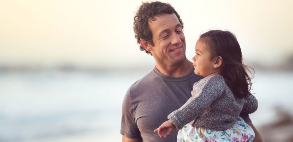 Un père tenant sa fille dans les bras sur la plage - santé mentale Un père tenant sa fille dans les bras sur la plage - santé mentale
