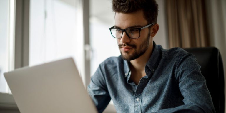 Un jeune homme barbu et portant des lunettes regardant le rapport sur la santé mentale en Europe sur son ordinateur