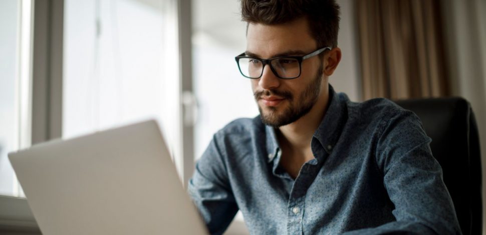 Un jeune homme barbu et portant des lunettes regardant le rapport sur la santé mentale en Europe sur son ordinateur