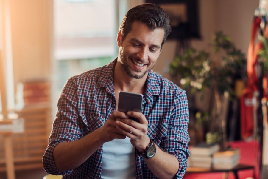 Un homme assis sur son bureau et utilisant son téléphone chez lui pour en apprendre plus sur les versements volontaires