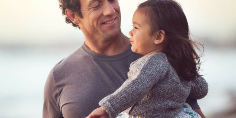 Un père tenant sa fille dans les bras sur une plage - protection sociale internationale des salariés expatriés