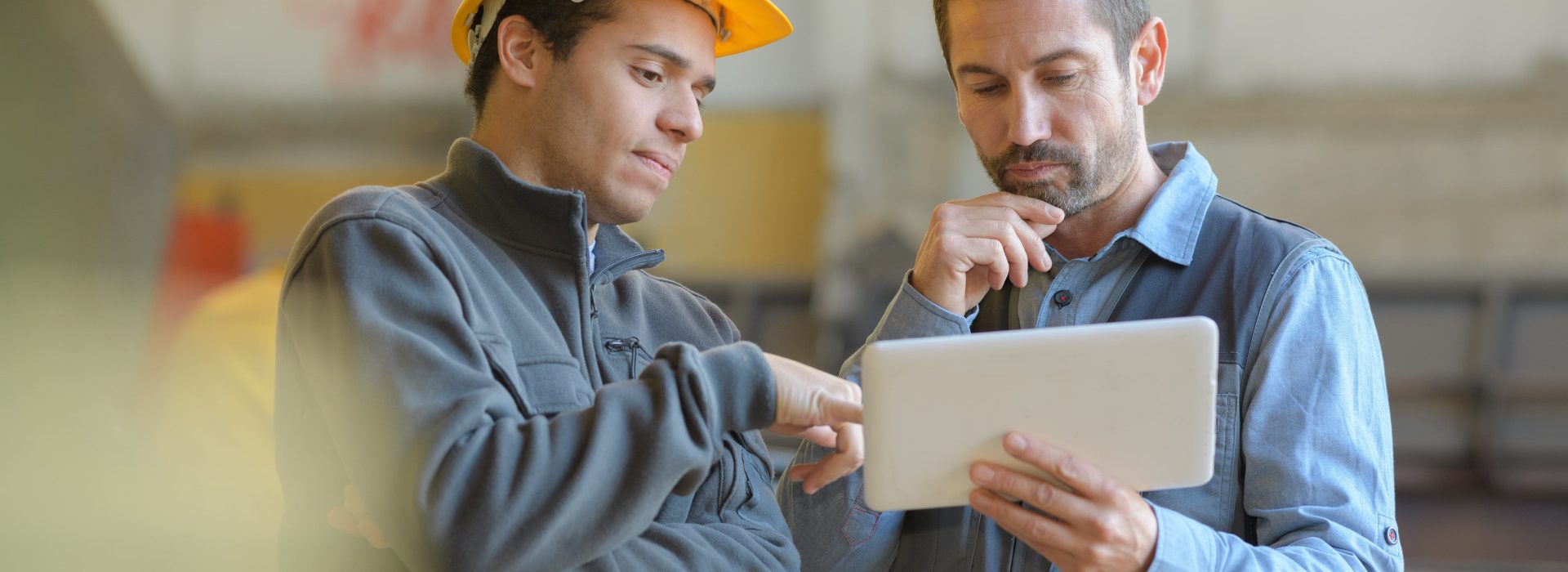 Deux hommes sur un chantier discutant avec une tablette à la main - aide au retour à l'emploi