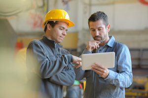 Deux hommes sur un chantier discutant avec une tablette à la main - aide au retour à l'emploi