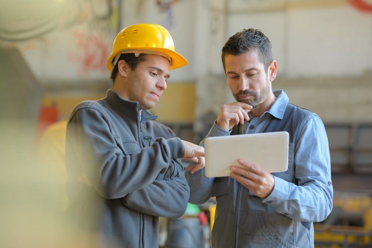 Deux hommes sur un chantier discutant avec une tablette à la main - aide au retour à l'emploi
