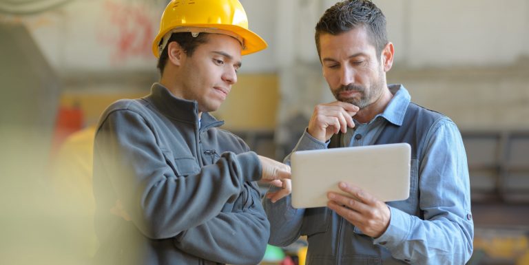 Deux hommes sur un chantier discutant avec une tablette à la main - aide au retour à l'emploi