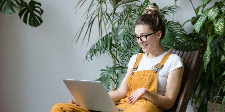 Une femme en salopette jaune et portant des lunettes est assise dans son fauteuil, sa tablette à la main, regardant les avantages du réseau Itelis