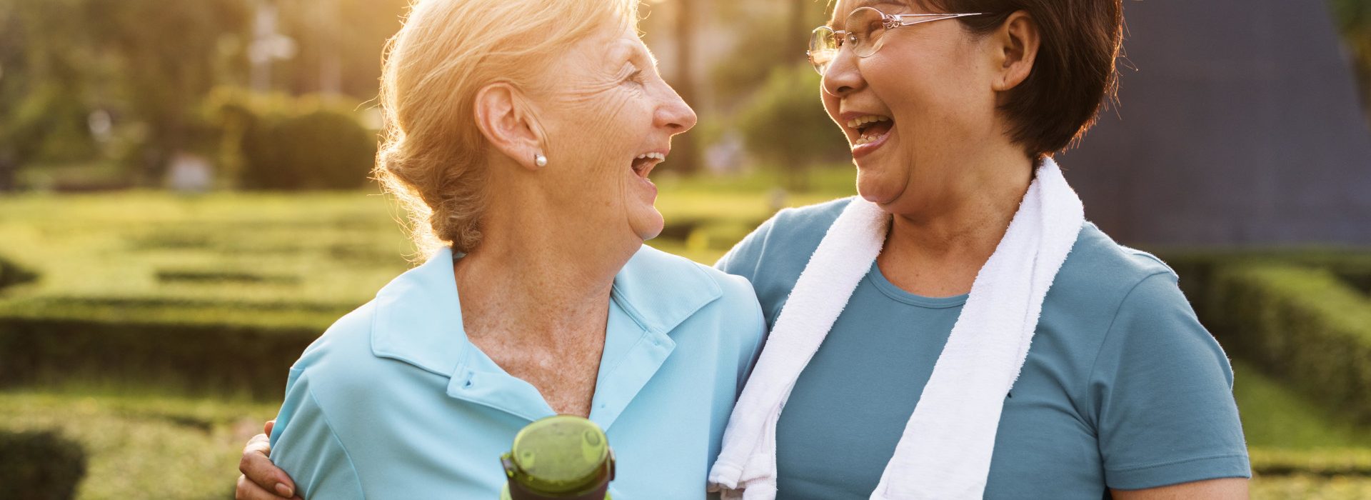 Deux femmes seniors rigolant après avoir fait du sport, l'une avec une serviette et l'autre avec une gourde à la main