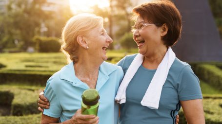 Deux femmes seniors rigolant après avoir fait du sport, l'une avec une serviette et l'autre avec une gourde à la main