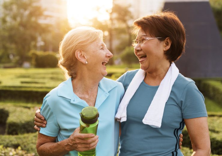 Deux femmes seniors rigolant après avoir fait du sport, l'une avec une serviette et l'autre avec une gourde à la main