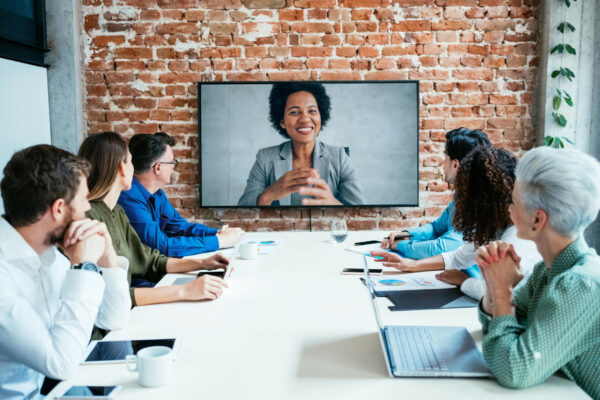 Des hommes et des femmes en réunion au bureau devant un écran projetant une femme en viso conférence - ressources humaines entreprises