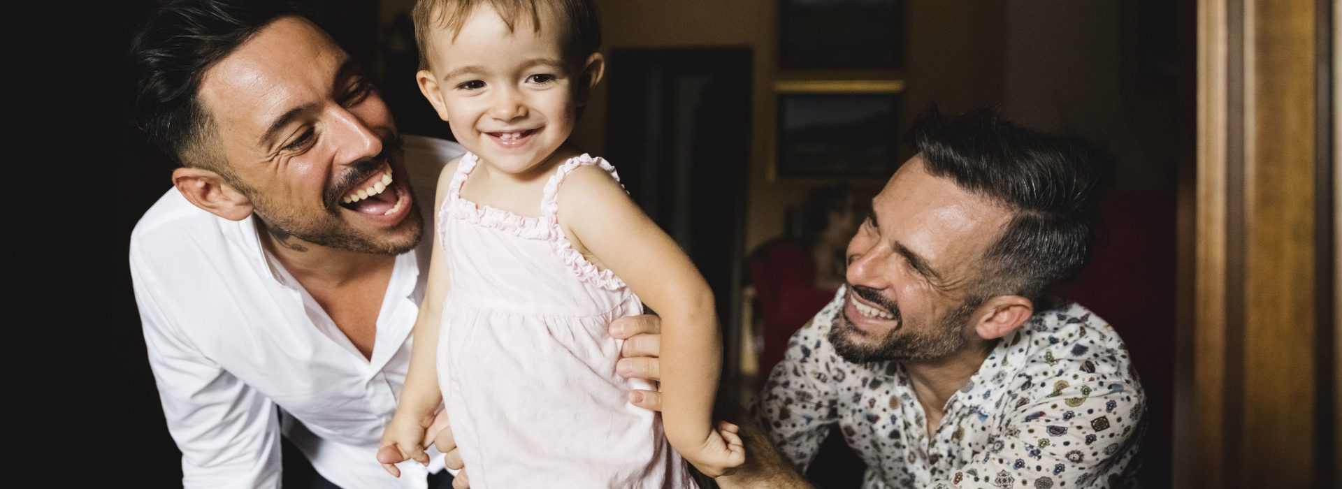 Deux hommes souriants et jouant avec leur petite fille - quijeprotege