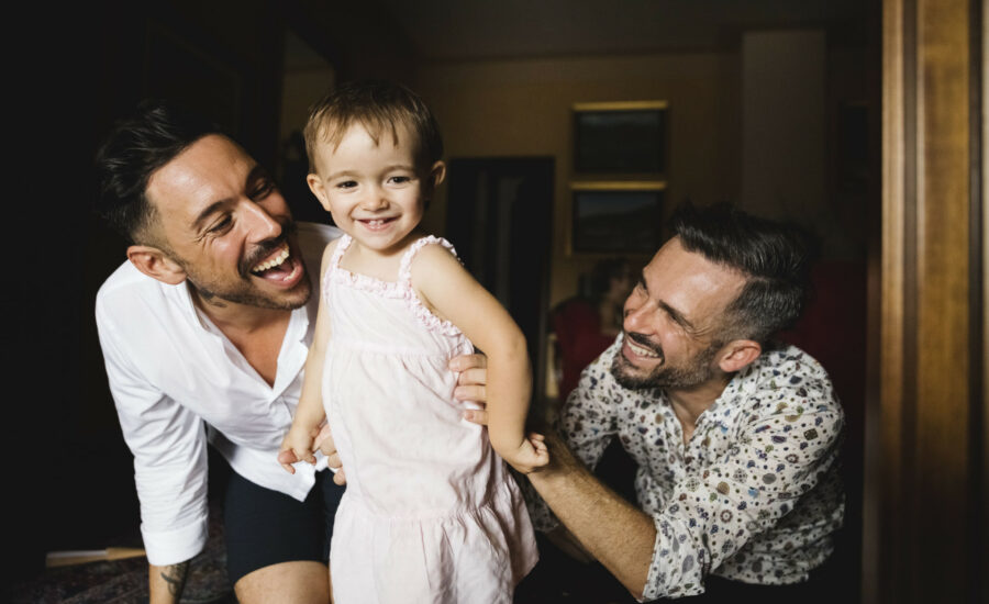 Deux hommes souriants et jouant avec leur petite fille - quijeprotege