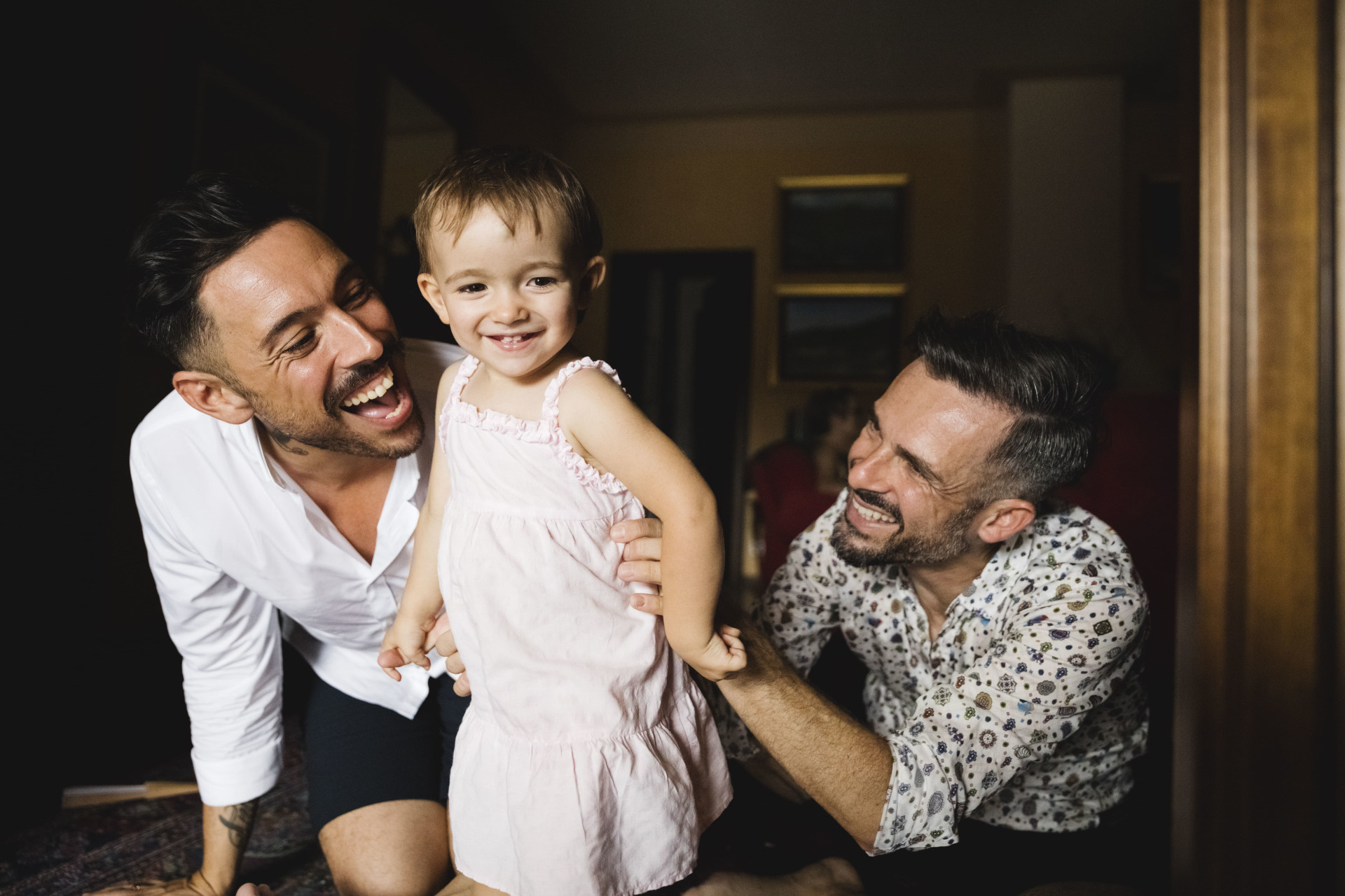 Deux hommes souriants et jouant avec leur petite fille - quijeprotege