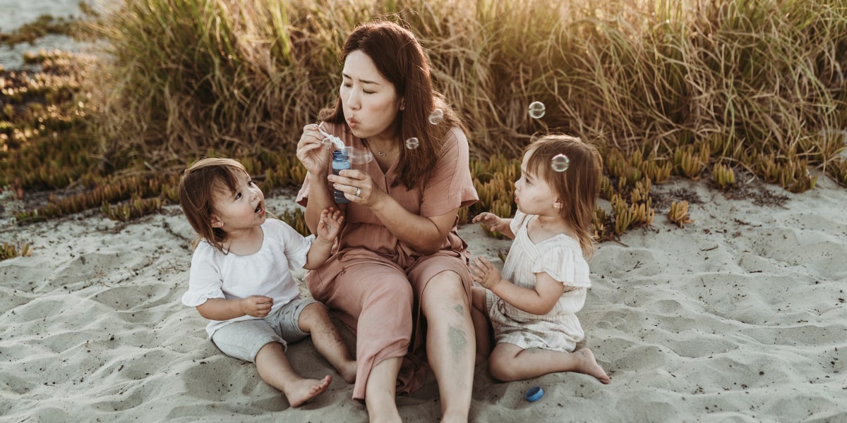 Une femme faisant des bulles avec ses deux enfants sur la plage - santé mentale